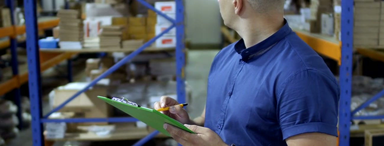 Factory worker checking inventory on a clipboard beside packed goods
