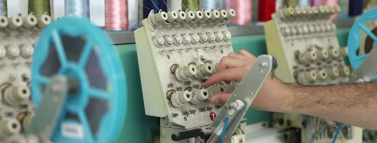 Operator adjusting thread controls on an industrial multi-thread sewing machine